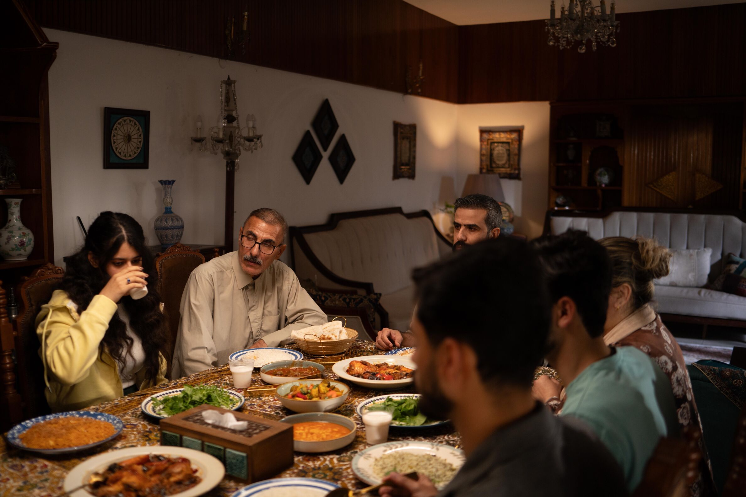 Family of several generations sharing iftar dishes around a long table in a warmly lit home