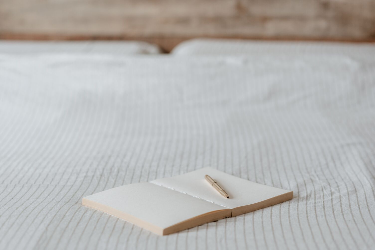 Open blank notebook with a pencil on a white bed sheet