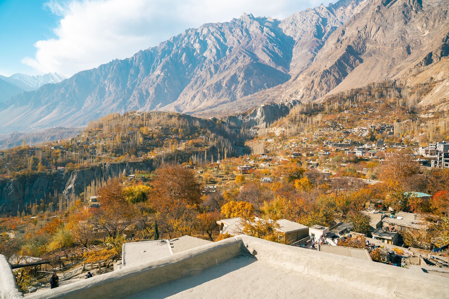 Autumn valley with orange trees and stone houses under bare mountains in northern Pakistan